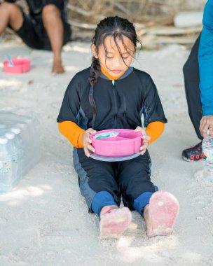 Çocuk sahilde piknik yaparken beslenme çantasından yemek yiyor..