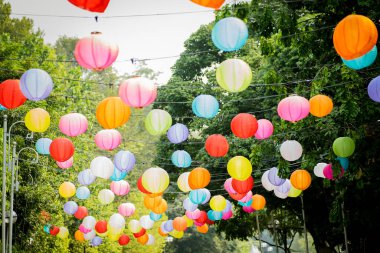 Arkaplanda ağaçlar ve gökyüzü asılı renkli kağıt fener..