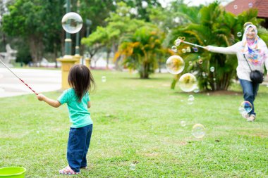 Parkta sabun köpüğüyle oynayan sevimli aktif Asyalı kız.