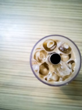 Buzlu kahveyle dolu bir bardak üzerinde, yeniden kullanılabilir bir metalle, ahşap bir restoranın masasında pipet içerken yaklaş.