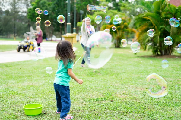 Parkta sabun köpüğüyle oynayan sevimli aktif Asyalı kız.