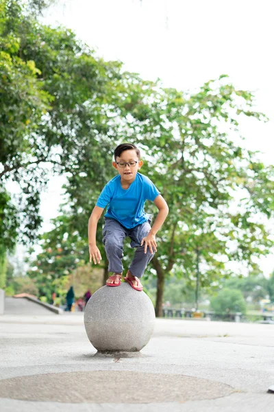 公園のコンクリートのボールからジャンプしようとしているかわいいマレーシアの男の子の屋外の肖像画 — ストック写真