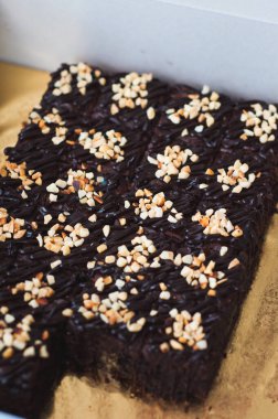 Tahta arka planda, üzerinde badem uçları, ev yapımı fırın ve tatlı olan plastik bir kapta çikolatalı brownie.