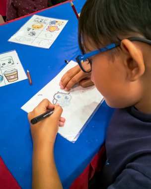 Kuala Lumpur, Malezya - Kasım 2019: Geri dönüşümlü plastik bir konteynır örtüsüne çizim yapan genç bir çocuğun yüksek açılı yakın çekimi. Anahtarlık yapıyorum..