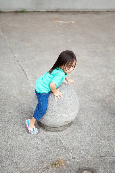 A toddler child sitting on the concrete sphere ball shape in the park.