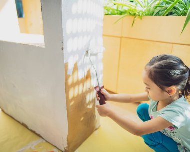 Küçük bir kızın beyaz boyalı ve silindirli kartonunu boyamak..