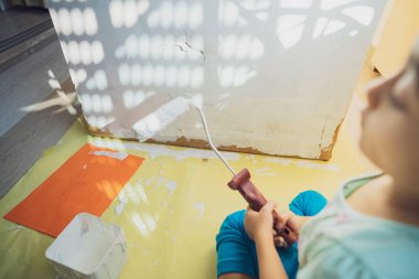 Küçük bir kızın beyaz boyalı ve silindirli kartonunu boyamak..