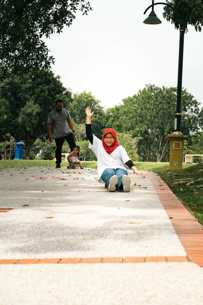 ヒジャーブを着た少女がスケートボードに座っている 公園の家族 — ストック写真