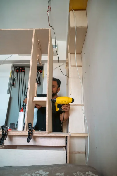 Building a wardrobe. Man using Framing Nailer to attach wooden plywoods.