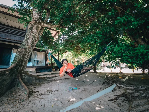 携帯電話を使用しながらハンモックでリラックスしたカジュアルな服装で幸せなアジアのティーンエイジャー ソーシャルメディア — ストック写真