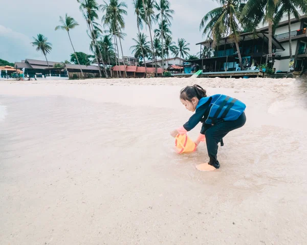 ライフジャケットを着た女の子が砂浜で砂を遊んでいます — ストック写真