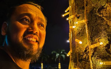 Milyar yaşında, sakallı Asyalı bir adam parktaki kurşun ampul ağacının yanında duruyor..