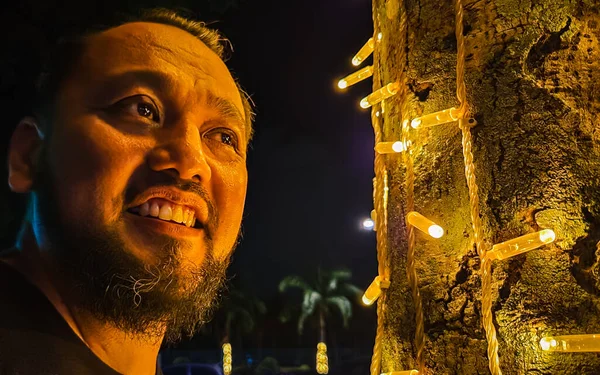 Milyar yaşında, sakallı Asyalı bir adam parktaki kurşun ampul ağacının yanında duruyor..