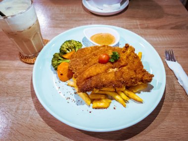 Kızartmaların ve lezzetli sebzelerin üzerinde servis edilen çıtır tavuk pirzolasının yakın çekimi..