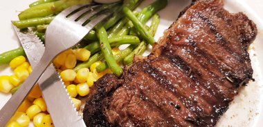 Dünyanın en iyi yemeklerini yemenin sevinci yanında patates püresi, mantar sosu ve tatlı mısırla birlikte beyaz tabakta servis edilen yeşil fasulye.