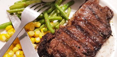 Dünyanın en iyi yemeklerini yemenin sevinci yanında patates püresi, mantar sosu ve tatlı mısırla birlikte beyaz tabakta servis edilen yeşil fasulye.