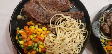 The best food in the world beef steak along with fried potatoes with delicious mushroom sauce and salad and spaghetti plated in beautiful black plate
