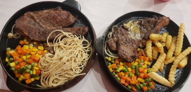 The best food in the world beef steak along with fried potatoes with delicious mushroom sauce and salad and spaghetti plated in beautiful black plate