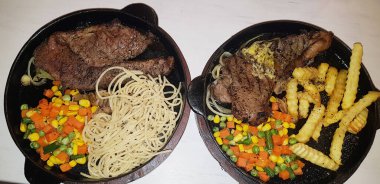 The best food in the world beef steak along with fried potatoes with delicious mushroom sauce and salad and spaghetti plated in beautiful black plate