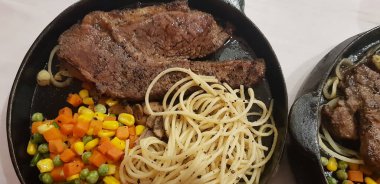 The best food in the world beef steak along with fried potatoes with delicious mushroom sauce and salad and spaghetti plated in beautiful black plate