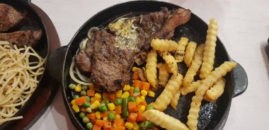 The best food in the world beef steak along with fried potatoes with delicious mushroom sauce and salad and spaghetti plated in beautiful black plate