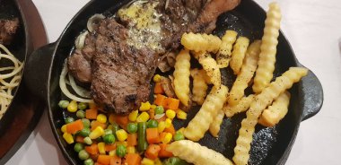 The best food in the world beef steak along with fried potatoes with delicious mushroom sauce and salad and spaghetti plated in beautiful black plate