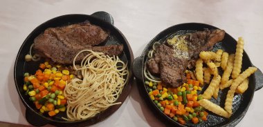 The best food in the world beef steak along with fried potatoes with delicious mushroom sauce and salad and spaghetti plated in beautiful black plate
