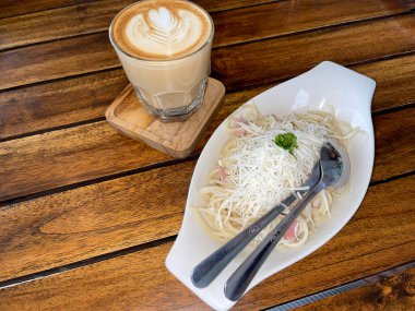 beautiful cup of cappuccino coffee with latte art and spaghetti alla carbonara in white plate with wooden space background