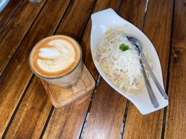 beautiful cup of cappuccino coffee with latte art and spaghetti alla carbonara in white plate with wooden space background