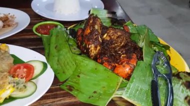 Delicious Indonesian seafood crab dish cooked with spices and seasoning sauce wrapped in banana leaf plate with other background dishes in Indonesian restaurant stock video