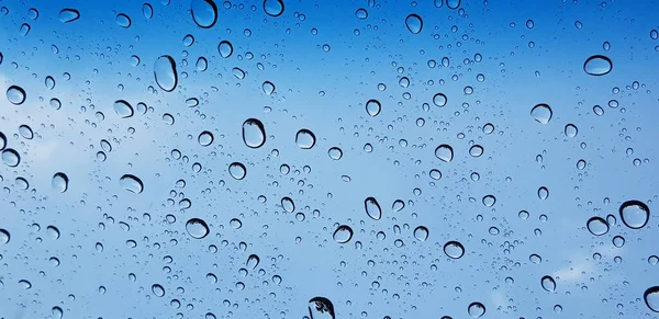 Water droplets perspective through window glass surface against blue sky good for multimedia content backgrounds