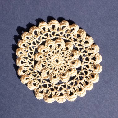 Handmade crochet lace in beige for placemats on a royal blue background. Flat lay.