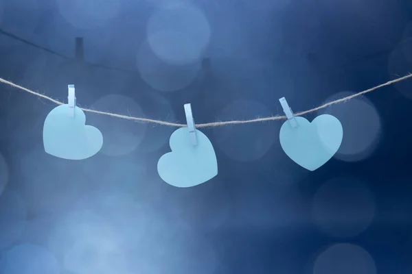Sticky notes in the shape of a blue heart, hung on a twine with blue wooden clips. Bokeh hearts on a blue background.