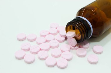 Beyaz arka planda izole edilmiş bir şişe tablet ve pembe tabletler.