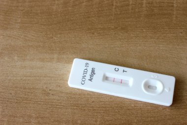 Tahta masa arkasındaki Covid-19 antijen test kitinin pozitif test sonucu