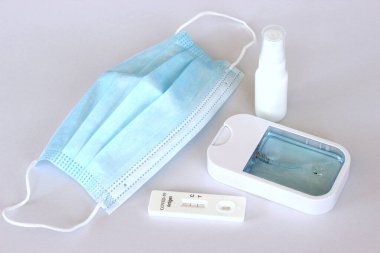 Maske, alkol spreyi ve beyaz arka planda Covid-19 antijen test kitinin pozitif test sonuçları.