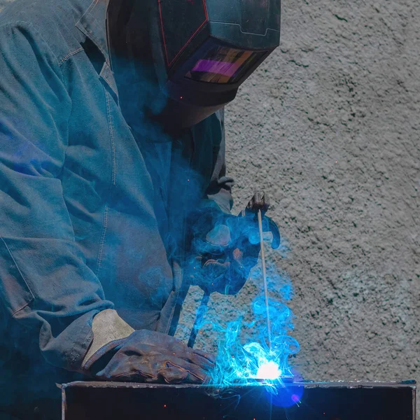 A welder in a protective mask welds a metal product with an electrode