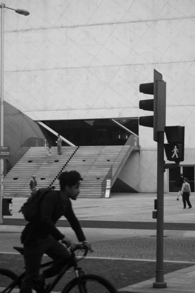 El estilo de vida urbano en monocromo - Edificio moderno y un ciclista que pasa en un desenfoque, un semáforo y la carretera de la ciudad - Foto calle en blanco y negro — Foto de Stock