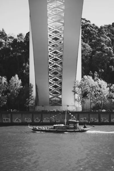 Porto, Portugalia - 18 września 2021: Pod mostem Arrabida nad brzegiem rzeki Douro przepływa łódź turystyczna przechodząca przez ścianę graffiti - czarno-biała — Zdjęcie stockowe