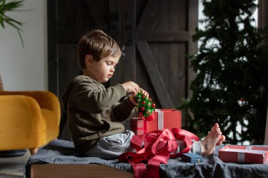 Küçük çocuk masada oturuyor ve evde Noel hediyeleriyle oynuyor. 