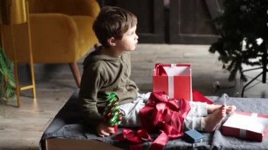 Küçük çocuk masada oturuyor ve evde Noel hediyeleriyle oynuyor. 