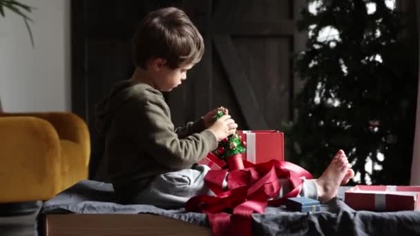 Liten Pojke Sitter Vid Bordet Och Leka Med Julklappar Hemma — Stockvideo