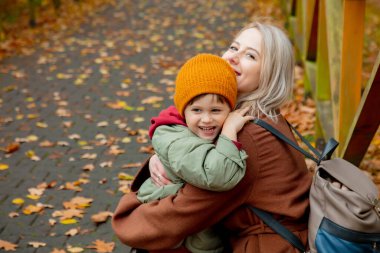 Anne ve oğlu sonbahar parkında sarılıyorlar.