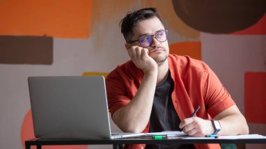 Masada dizüstü bilgisayar ve not defteriyle çalışan bir adam.