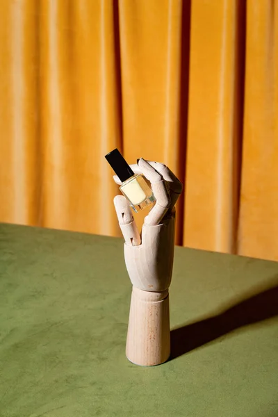 Wooden human hand hold nail polish on yellow curtains background