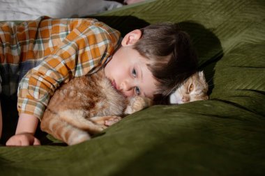 Küçük çocuk yatakta bir kediye sarılıyor. 