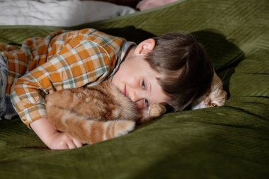 little boy hugging a cat lying on the bed 