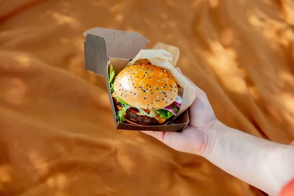 Mężczyzna Ręka Trzymać Smaczny Burger Pudełku Brązowy Kolor Tkaniny — Zdjęcie stockowe