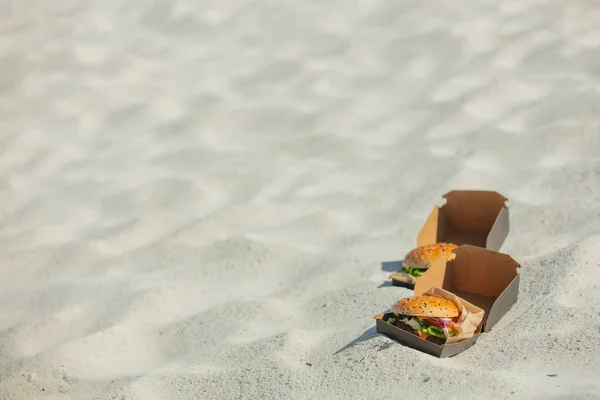 Tasty burger in box on white sand on beach