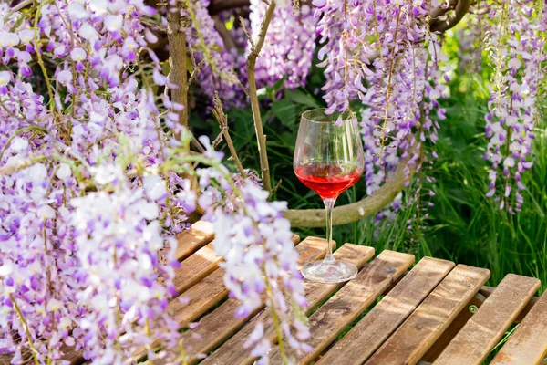 Glass of wine on wooden table near wisteria tree